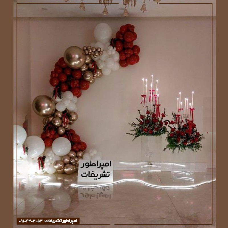 بادکنک آرایی قرمز و سفید طلایی با گل آرایی رز قرمز و شمع‌های بلند سفید