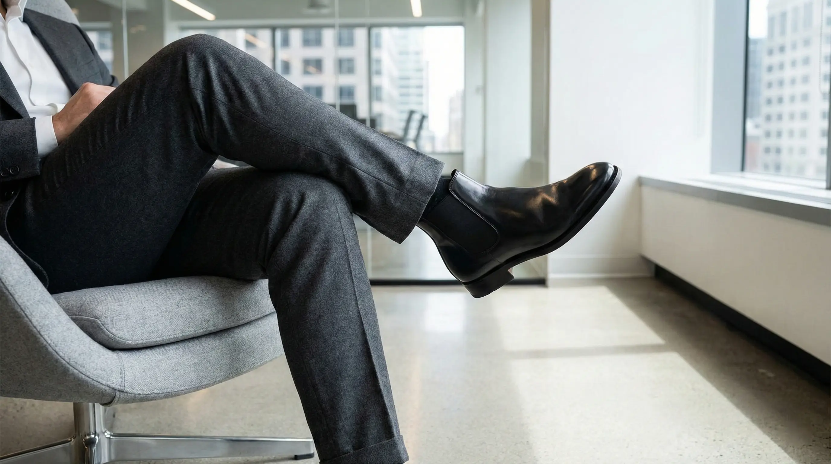 مردی با نیم بوت چلسی چرم مشکی براق و شلوار پارچه&zwnj;ای در محیط اداری مدرن، استایل رسمی و راحت.