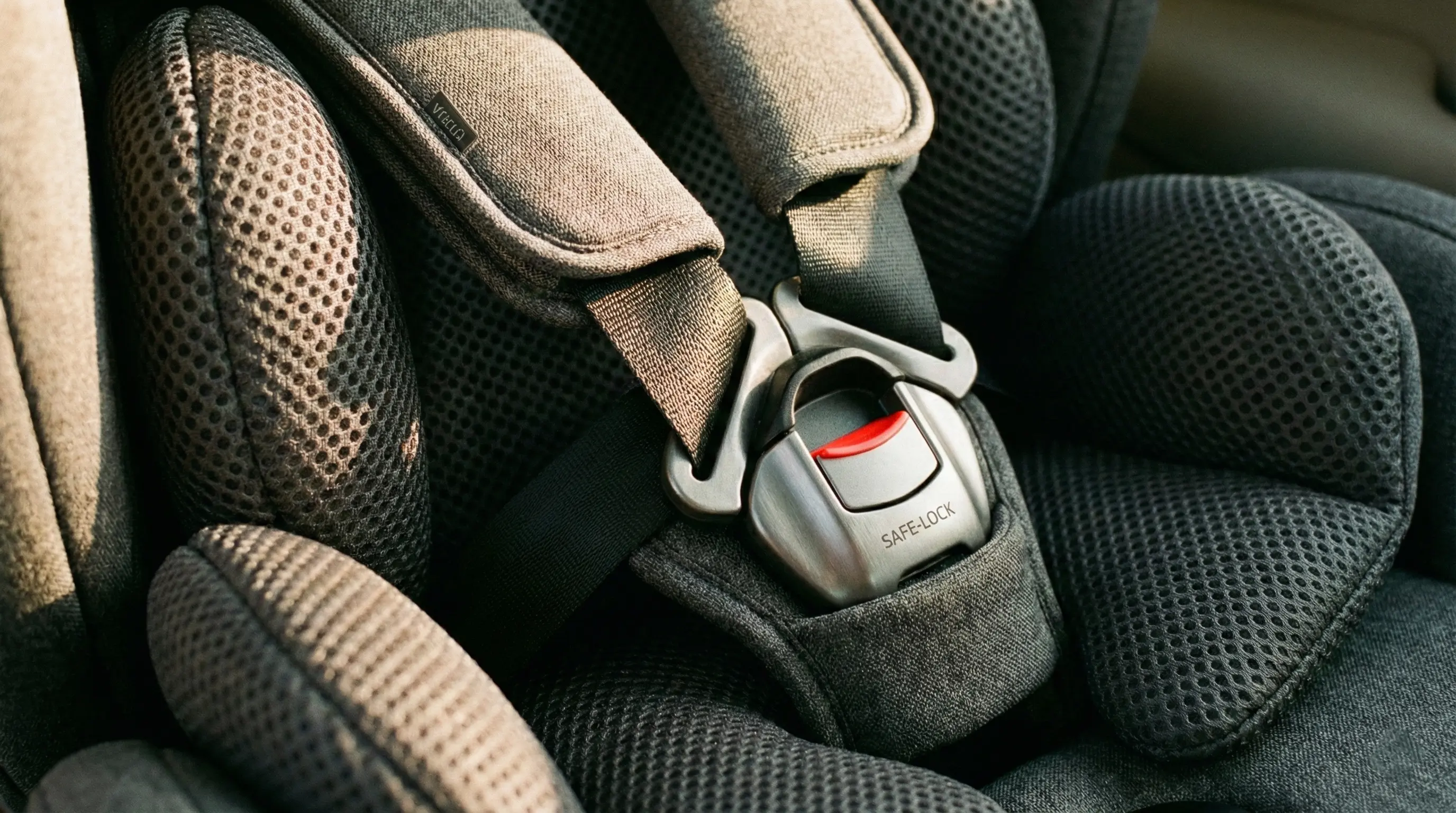 A macro close-up detail shot of the safety buckle and the side protection padding of a high-quality baby car seat. The focus is on the sturdy construction of the buckle and the breathable mesh texture of the fabric. The image conveys "high safety standards" and "durability." Soft, warm lighting. Aspect Ratio: 16:9